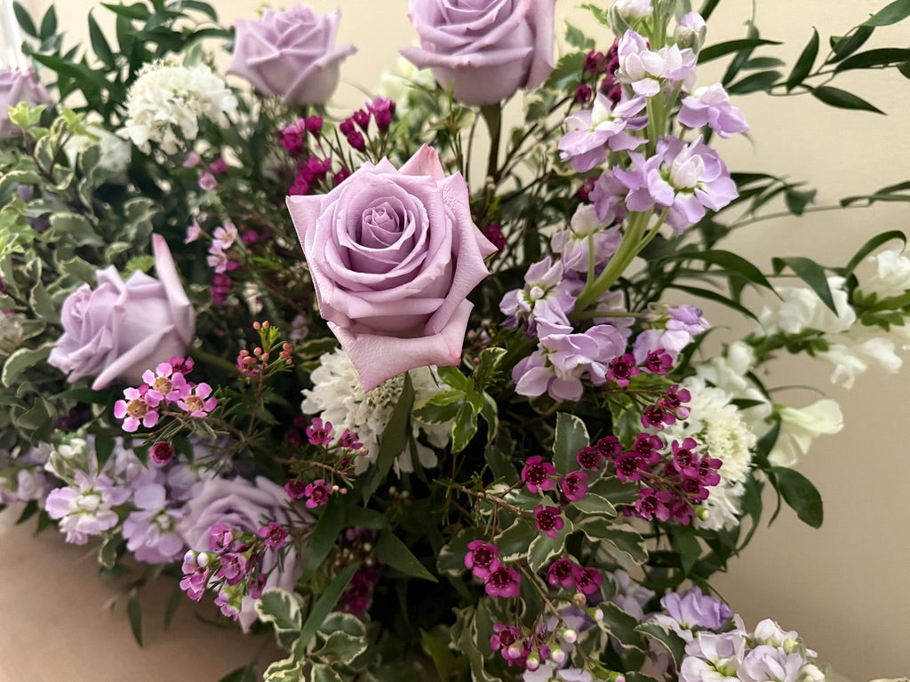 Lush floral design with purple and white roses, stock, wax flower, scabiosa and snapdragon.