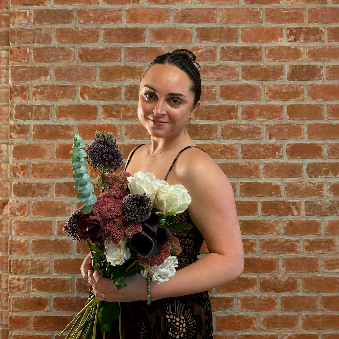 Founder, Liz, holding a bouquet of loose flowers in front of a brick wall.